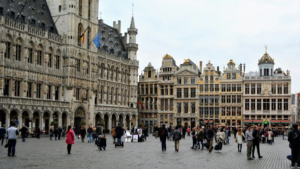 Main square in the city of Antwerp, Belgium. The Belgian and European flags are flying on the main monument. The photo was taken in autumn or winter, judging by the clothing of the people walking around the square.
