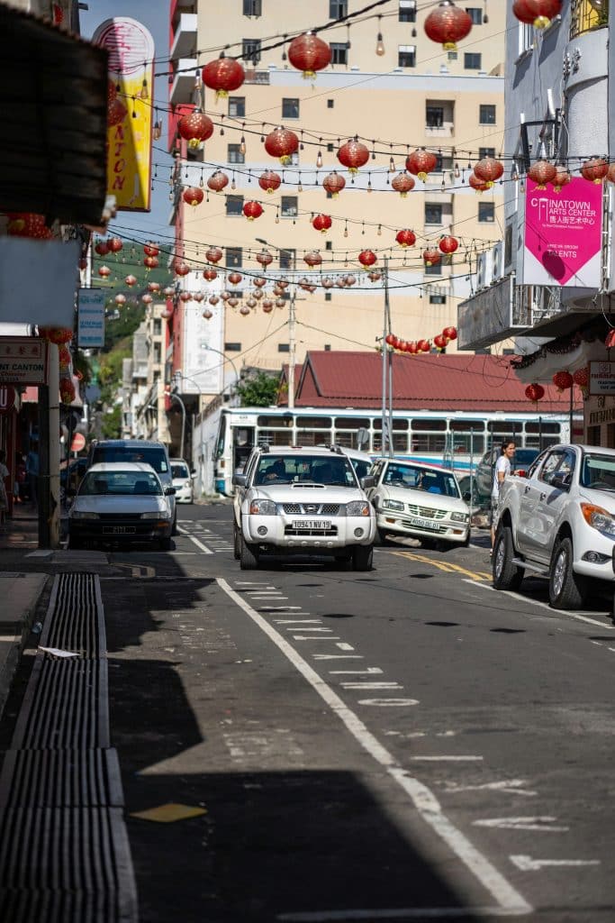 A car drives down an avenue in Chinatown in Port Louis, Mauritius. Red lanterns hang in the street.