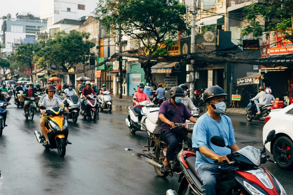 Motorcycles driving down a street in Ho Chi Minh City, Vietnam. Several motorcyclists are wearing surgical masks to protect themselves from pollution.