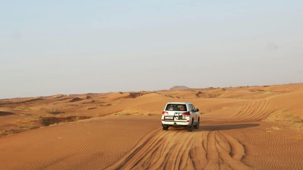 A small van drives through the African desert. It is alone in the landscape.