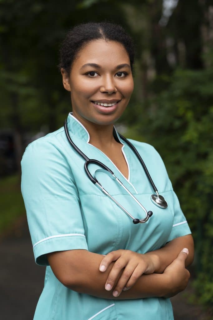 Vertical portrait of a nurse in the Seychelles in her work uniform. She is wearing a stethoscope around her neck and smiling with her arms crossed.