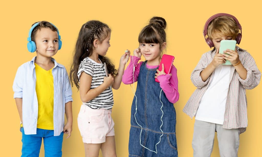 A group of four young children on a yellow background are listening to music through headphones and earphones. The two girls are sharing their earphones and the two boys each have a pair of headphones.