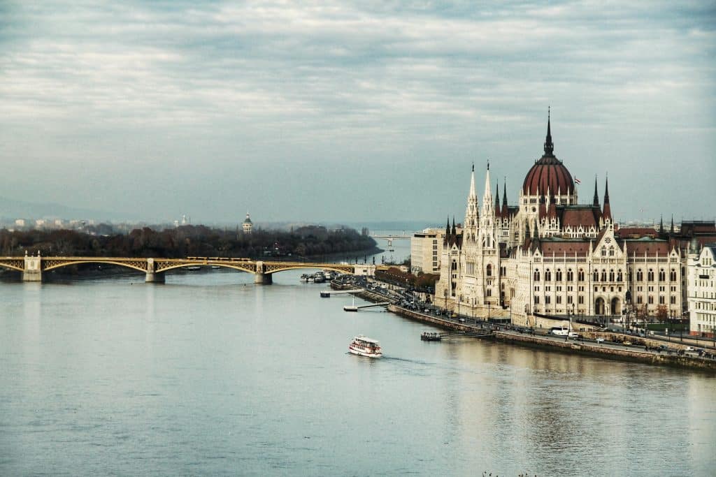 Vintage photo of Budapest and the river running through the city, with its bridge and historic monument reflected in the water. The sky is grey.
