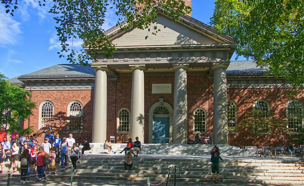 A group of people are standing in front of Harvard University in Massachusetts, USA, on a sunny day.